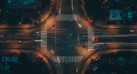 An aerial top-down view of a city street intersection at night with long exposure light trails from moving cars.