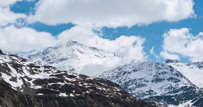 Majestic snow-capped peaks of Montespluga under blue sky with white clouds, Italian Alps, Italy. Time-lapse motion-lapse