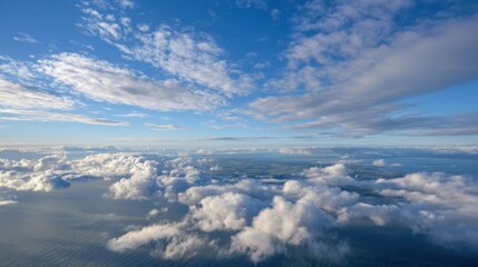 An expansive sky showcases fluffy white clouds above the deep blue ocean, illuminated by bright sunlight. The scene captures a serene atmosphere with hints of land in the distance.