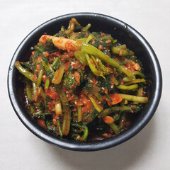 A close-up image of a black bowl filled with spicy Korean young radish kimchi, or 