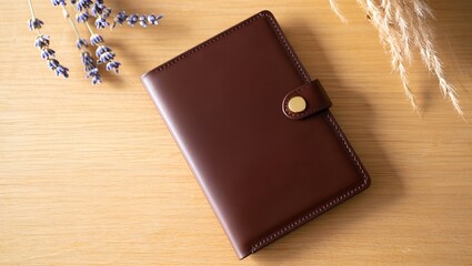 Brown leather planner with a button closure rests on a light wood surface, elegant and simple.