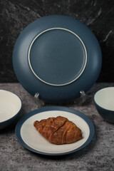 A fresh croissant served on a modern blue and white ceramic plate. The dinnerware set has a stylish matte finish. Perfect for bakery or cafe concepts.
