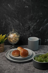 Breakfast scene with bread rolls on a gray ceramic plate, green grapes in a bowl, and a mug. Cozy and rustic food photography concept.