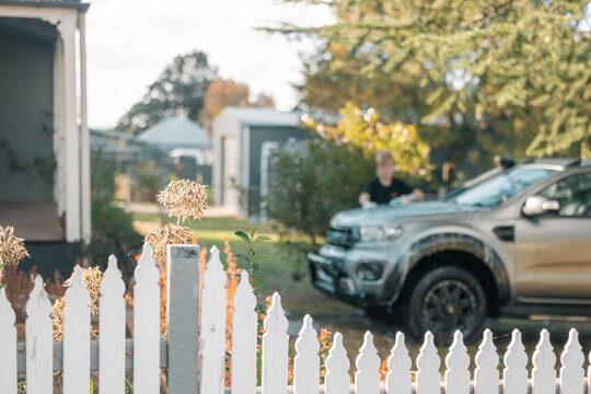 Garden along white picket fence of home with boy washing car in background