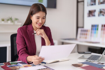 Adult Asian professional reviews design documents and material samples in a bright modern office workspace