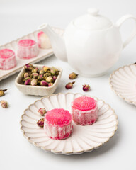 Homemade Chinese snow skin mooncakes. Snowy Moon cakes with Rose Bud Tea and White Teapot on White Background. Mid-Autumn Festival, traditional Asian desserts, and seasonal celebrations in Asian count