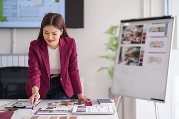 Asian adult woman architect working on interior design plans reviewing blueprints material samples for home property real estate projects in a modern office