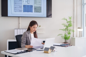 Asian real estate professional woman reviews property documents in modern office architect sales...