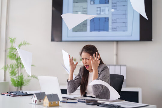 Asian adult professional woman overwhelmed work stress office chaos papers scatter architect real estate business challenges pressure deadlines