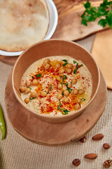 A delightful bowl of creamy hummus topped with chickpeas, paprika, and herbs served alongside crispy bread on a rustic wooden table.