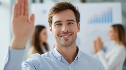 Confident young professional man smiling while raising his hand during business meeting or seminar in modern office. His colleagues are in background