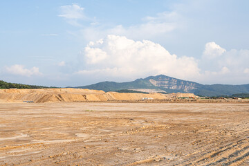 Expansive construction site with exposed earth and heavy machinery tracks. Surrounded by distant mountains, the scene captures early stages of land development and earthmoving operations.