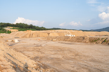 Expansive construction site with exposed earth and heavy machinery tracks. Surrounded by distant mountains, the scene captures early stages of land development and earthmoving operations.