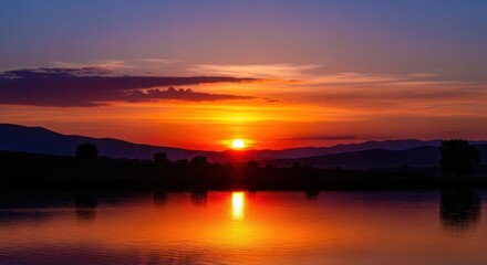 Serene sunset over lake with reflections and distant mountains silhouette