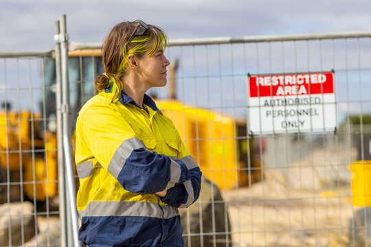 Woman in profile on worksite wearing hi-vis in front of temporary fencing