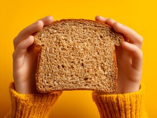 Human hands gently holding a slice of whole grain toast against a vibrant yellow background for healthy eating.