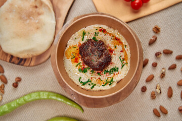 A Scenic Display of Hummus Topped with Spiced Meatball Garnished with Green Herbs, Surrounded by Fresh Vegetables and Nuts on a Rustic Table Setting