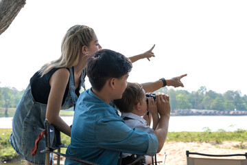 Fototapeta premium Asian family teaching boy using binocular doing bird watching on summer camping