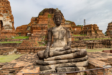 Ancient Buddha statue in front of ruined brick structures at Wat Phra Ram, Ayutthaya, Thailand