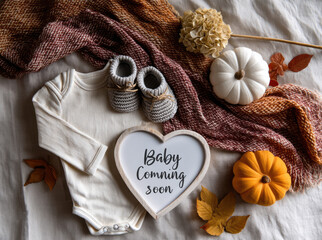 Baby coming soon autumn announcement with cream baby bodysuit, knitted booties, pumpkins, dried flowers, and cozy blanket on fabric