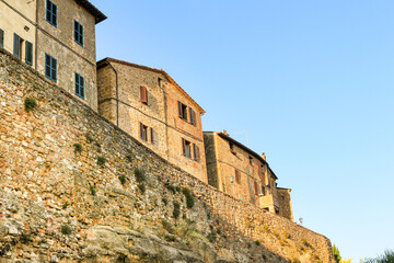 Italian homes on high city walls in Tuscany. towering over the road below, sat high on a yellow stone city wall.  Historic buildings with a clear blue sky behind. 