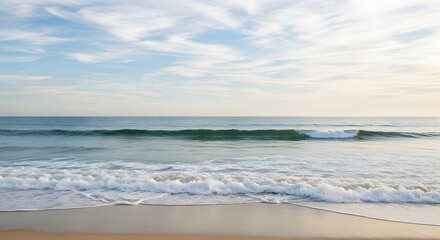 Fototapeta premium Ocean waves gently rolling onto a sandy beach under a cloudy sky