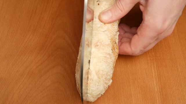 Baker cutting a loaf of bread in half lengthwise on a wooden cutting board