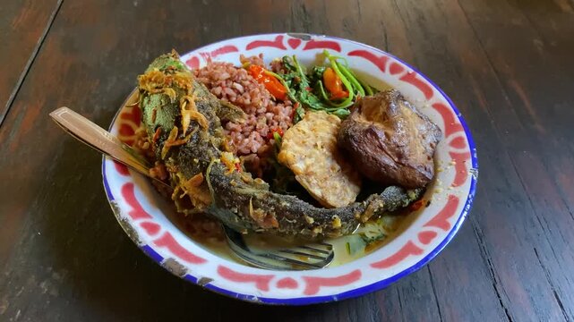 4k video footage of Mangut Lele is authentic javanese food from Yogyakarta and Solo. Traditional catfish dishes are full of spices and spicy in a plate on wooden table.