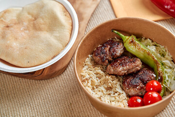 A Delicious Bowl of Grilled Meatballs Served with Rice, Fresh Vegetables, and Pita Bread for a Satisfying Meal Experience