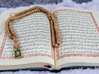 Holy Quran with arabic calligraphy meaning of Al Qur'an and tasbih or rosary beads on white velvet...
