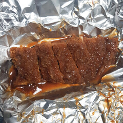 A close-up of a container of crispy fried pork cutlets (donkaseu) smothered in a sweet and savory sauce.
