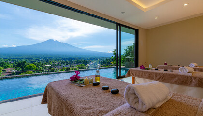 The image shows the interior of a luxurious spa with panoramic views of the mountains. The room has two massage tables, neatly draped with brown sheets and white towels. Massage and aromatherapy acces