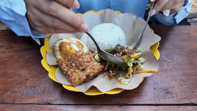 An Indonesian woman eating sego Pecel, the traditional dish from Java, Indonesia, consisting of boiled vegetables, peanut sauce, and side dishes.