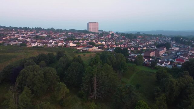 Retreating Aerial Shot of Large Giant Office Building Surrounded by Residential Houses at Sunrise with Green Trees and Fields in Park Nearby.
