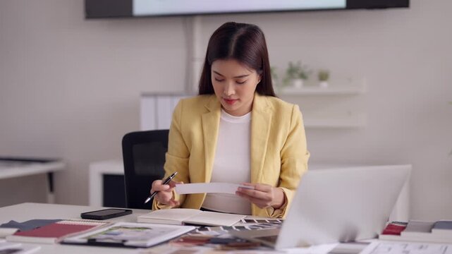 Asian adult woman architect diligently planning new building project in modern office workspace documents and design samples