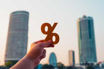 Holding a wooden percentage symbol, an investor stands amidst corporate buildings, a metaphor for...