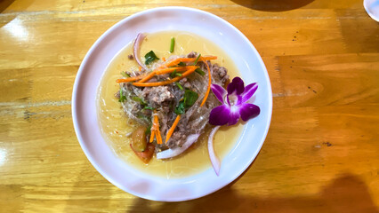Thai glass noodle salad with fresh herbs on a white ceramic plate, flat lay view.