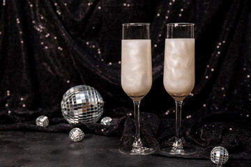 Two glasses of white New Year's cocktail with edible glitter on a black background, copyspace for text