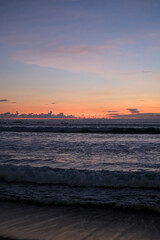 Golden sunset paints the sky over Kuta Beach, Bali, blending warm orange and purple hues above calm ocean waves, creating a serene and breathtaking view along the horizon of this tropical coast.