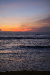 Golden sunset paints the sky over Kuta Beach, Bali, blending warm orange and purple hues above calm ocean waves, creating a serene and breathtaking view along the horizon of this tropical coast.