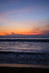 Golden sunset paints the sky over Kuta Beach, Bali, blending warm orange and purple hues above calm ocean waves, creating a serene and breathtaking view along the horizon of this tropical coast.
