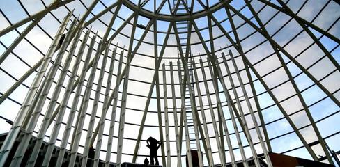 Silhouetted figures explore a modern architectural structure beneath a glass dome