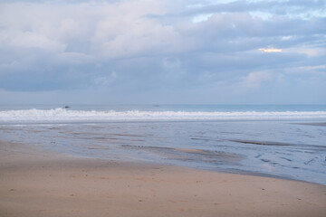 Peaceful morning atmosphere at Seminyak Beach, Bali, where soft waves meet wide stretches of sand under pastel skies, creating a serene coastal view with gentle colors and quiet reflections.