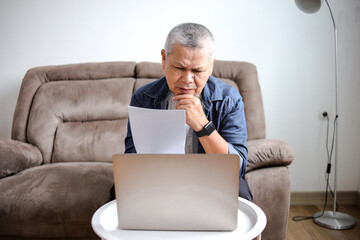 Portrait Old Asian Man Confused While Holding Document And Working On Laptop