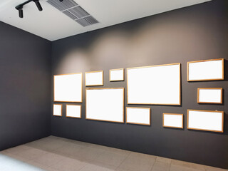 A collection of blank picture frames of various sizes is mounted on a dark gray wall inside a modern gallery or exhibition space. Copy space for your gallery photography.