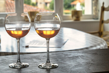 Two wine glasses are on a table.The table is in front of a window