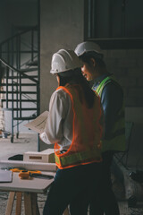 Construction manager and engineer dressed in orange work vests and hard helmets explore construction documentation on the building site near the steel frames