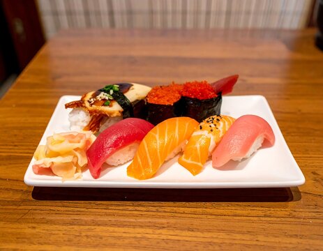 Assorted sushi pieces artfully arranged on a rectangular white plate, served on a wooden table