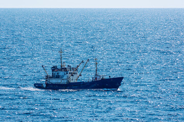 Fishing boat in blue sea and clear sky with birds flying overhead.