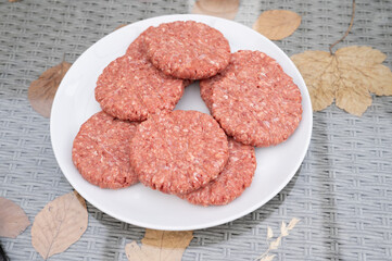 Raw ground beef patties on white plate with autumn leaves background